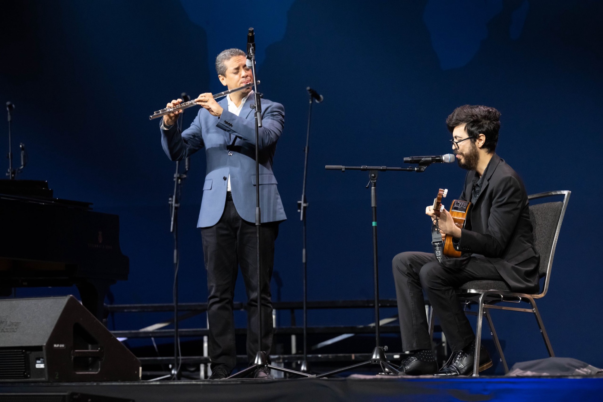 Felipe Paccagnella playing guitar and singing on stage next to a flutist