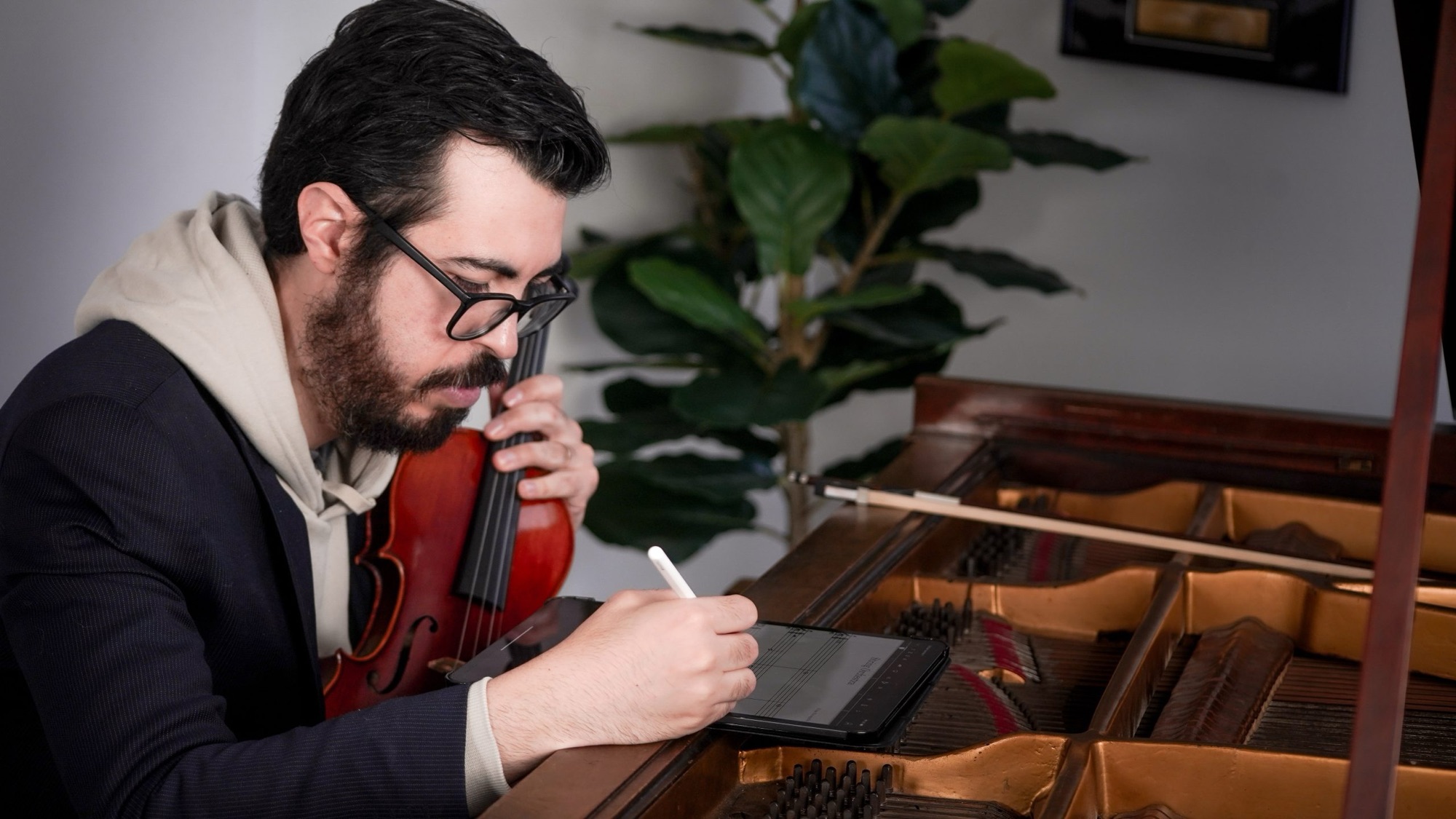 Felipe Paccagnella writing notation on a tablet while holding a violin, next to an open piano